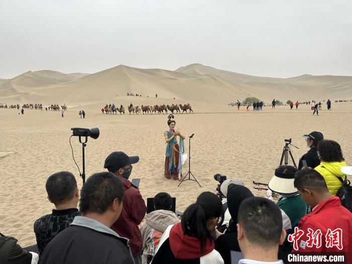 圖為2023年4月底，敦煌大漠“逐舞者”奧楠在鳴沙山月牙泉景區(qū)視頻直播，吸引游人圍觀?！●T志軍 攝